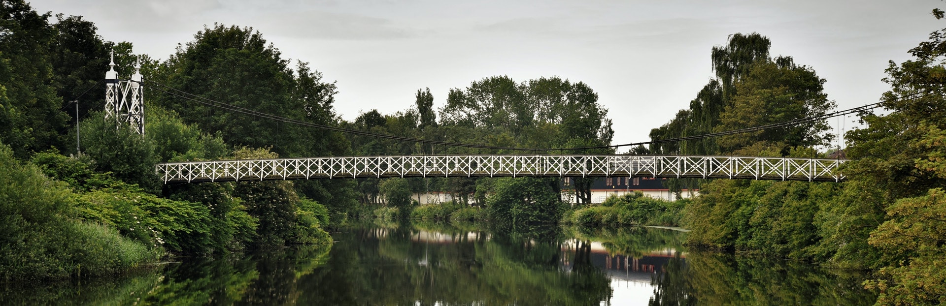 A suspension footbridge over a river in a park. Photograph of the Howley suspension footbridge in Warrington