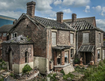 Abandoned and boarded up old house with missing roof tiles.