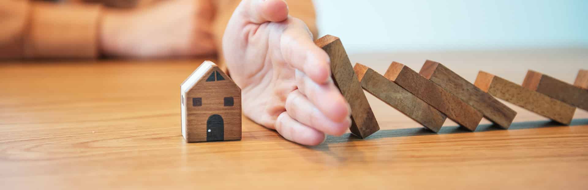 Blocks falling onto a toy house are blocked by a hand. Represents stopping a repossession.
