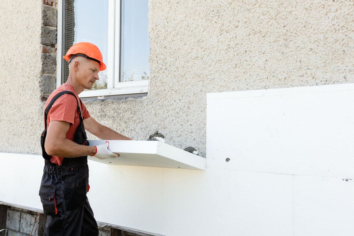 External Polyfoam Insulation A worker installing a styrofoam board on the facade of a house.