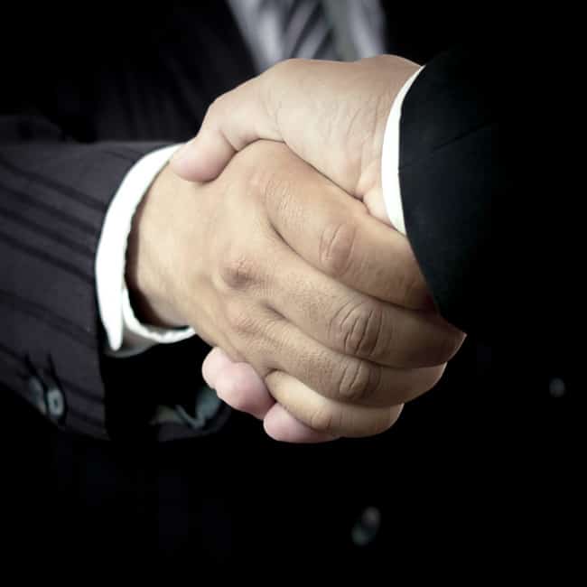 Two men in suits shake hands.