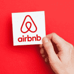 A hand holds up a white card with the Airbnb logo on it.