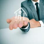 A businessman sitting in a desk showing a drawing of a house in his hand. Image represents a letting agent.