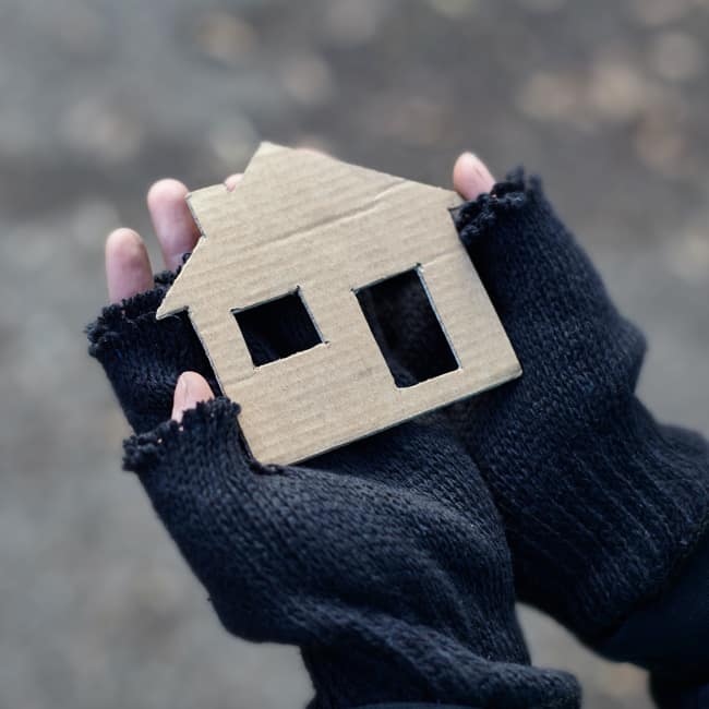 The gloved hands of a homeless boy hold a cardboard house.