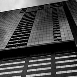 A black and white image, looking up at a modern skyscraper.