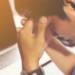 A man with his heads in his hands in front of a laptop.