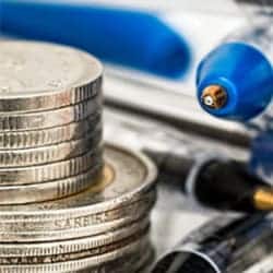 A pile of coins sits next to some pens. Image represents tax.