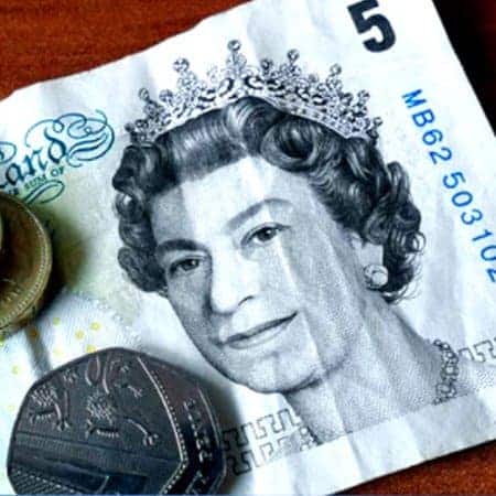 A close up photograph of a 5 pound note with some coins sitting on it.