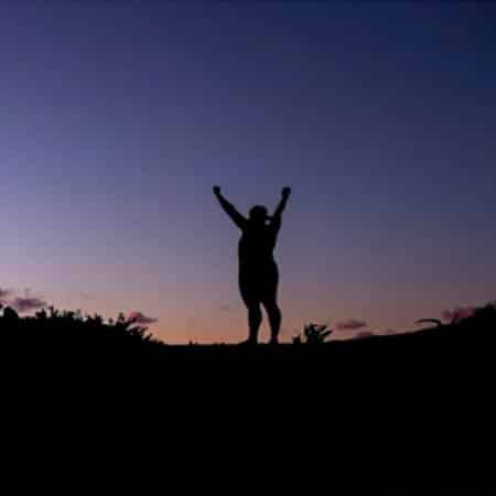 A silhouette of a man raising his hands to the sky.