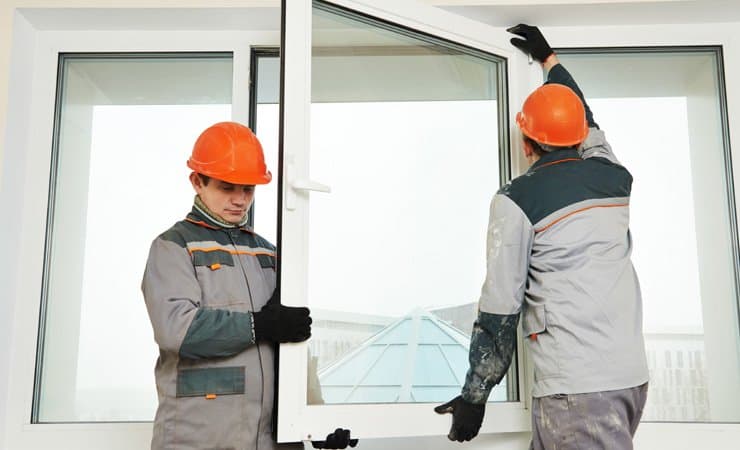 A photo of two male construction workers installing a window