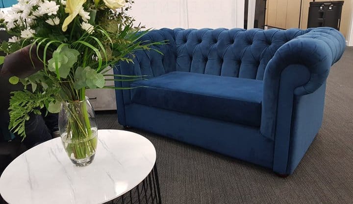 Photograph of a blue Chesterfield sofa with flowers in the foreground