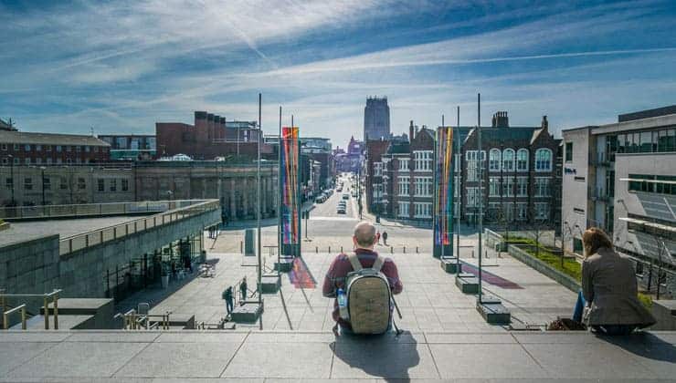 A man with a rucksack sits on some steps looking out at Liverpool city centre.