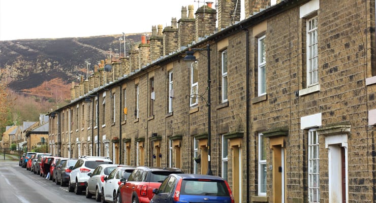 Stone terraced cottages with cars parked outside and a hill in the background. Photograph taken in Carrbrook, Tameside