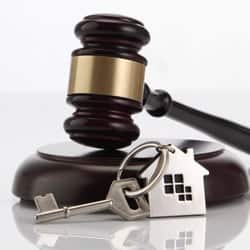 A auctioneer's block and gavel sit behind a set of house keys.