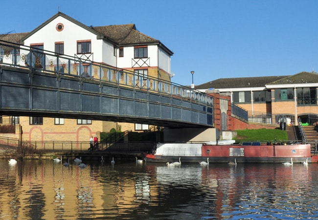 A footbridge over a river on a summer day. Photograph of a bridge over the River Nene in Peterbourough