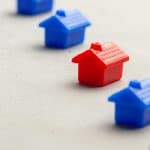 Four plastic, model houses in a row. Three are blue and one is red.