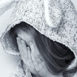 A young, homeless girl covering her face with her hands.