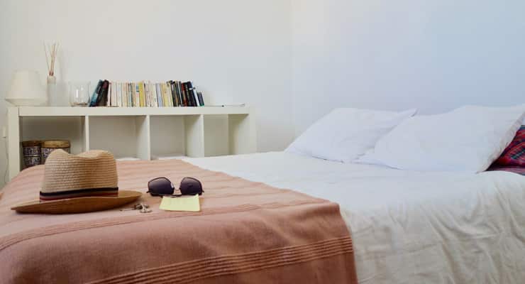 A hat rests on a bed with a brown and white bead spread. Style is reminiscent of an Airbnb listing