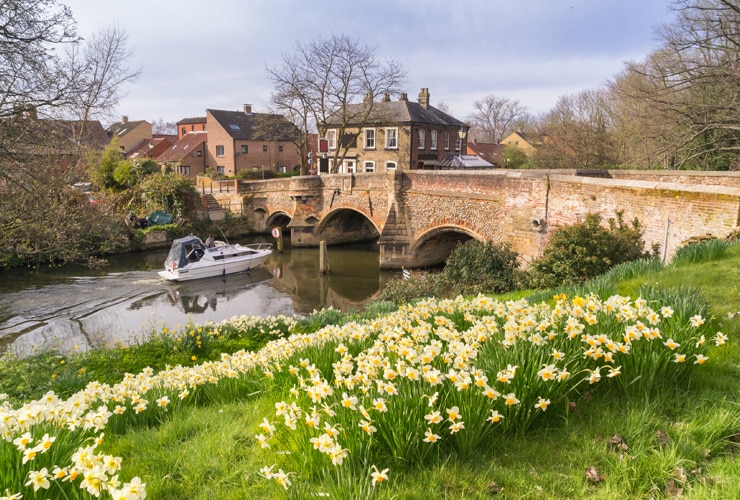 A boat travels along a river next to Bishopgate Bridge in Norwich.