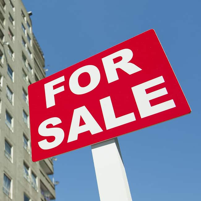 A for sale sign in the foreground and a block of flats in the background.