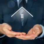 An estate agent in a business suit holds his hands out to reveal the image of a house.