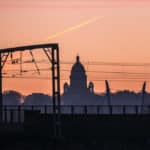 A silhouette of the Ashton Memorial in Lancaster against the sunset. In the foreground there is a train line.