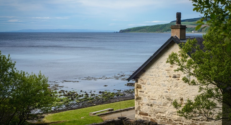 A stone holiday cottage in the foreground and the sea in the background. Photograph taken in Ayrshire on the on the west coast of Scotland