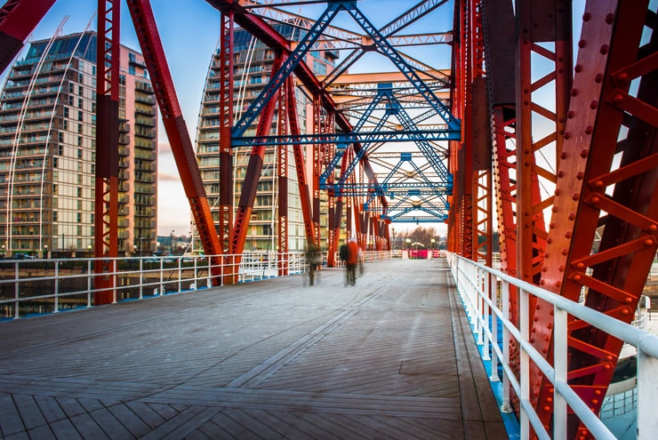 Photograph on a red industrial bridge with skyscrapers in the background. The Detroit Bridge in Salford