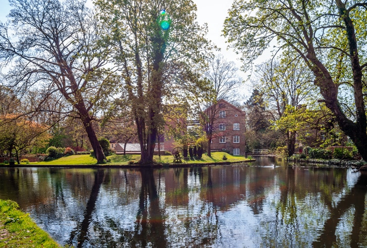 A picture of the Old Mill House at Grove Mill, Cassiobury Park. Old buildings seen through the trees and over the water on a summer day.