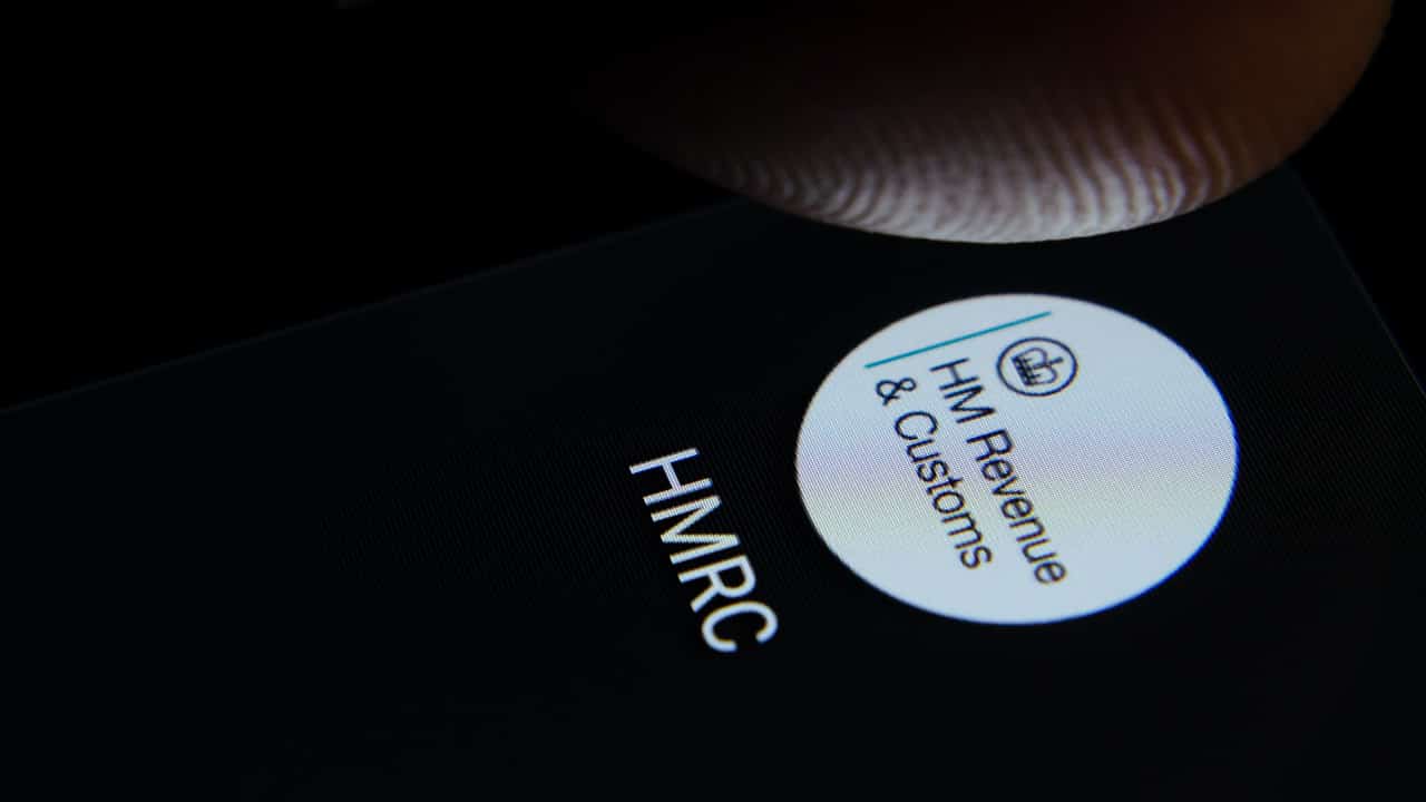 The HMRC logo can be seen on a phone screen, sitting next to a stone.