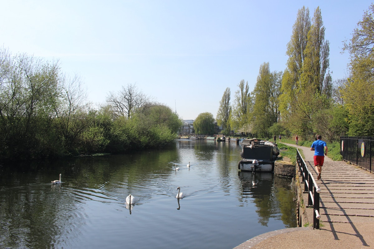 A jogger runs besides the River Lea on a clear blue day. Photograph taken near Tottenham Hale.