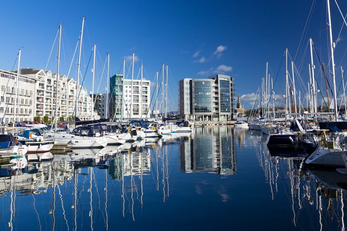 The marina in Plymouth with yachts along the waterfront and skyrise buildings in the background.