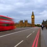 View over the Westminster Bridge with Big Ben in the background. A red bus going over the bridge is captured with a motion blur.