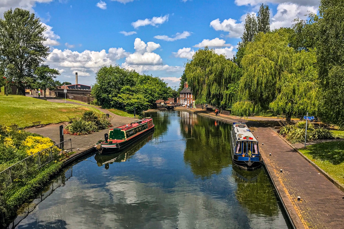 View of the Wolverhampton canal walk-way with a blue sky and reflected by the water and longboats moored at the edges.