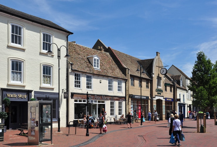 Shoppers walk about the marketplace in Ely on a bright sunny day.