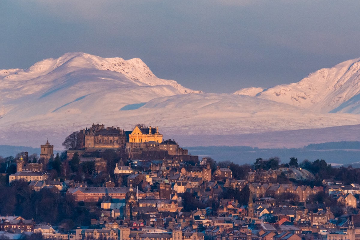 Stirling Castle in winter. The castle sits on a hill with snowy mountains in the background.