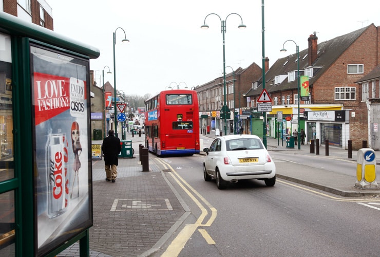 A red bus drives down a busy high street. Photograph taken in Borehamwood on the outskirts of London.