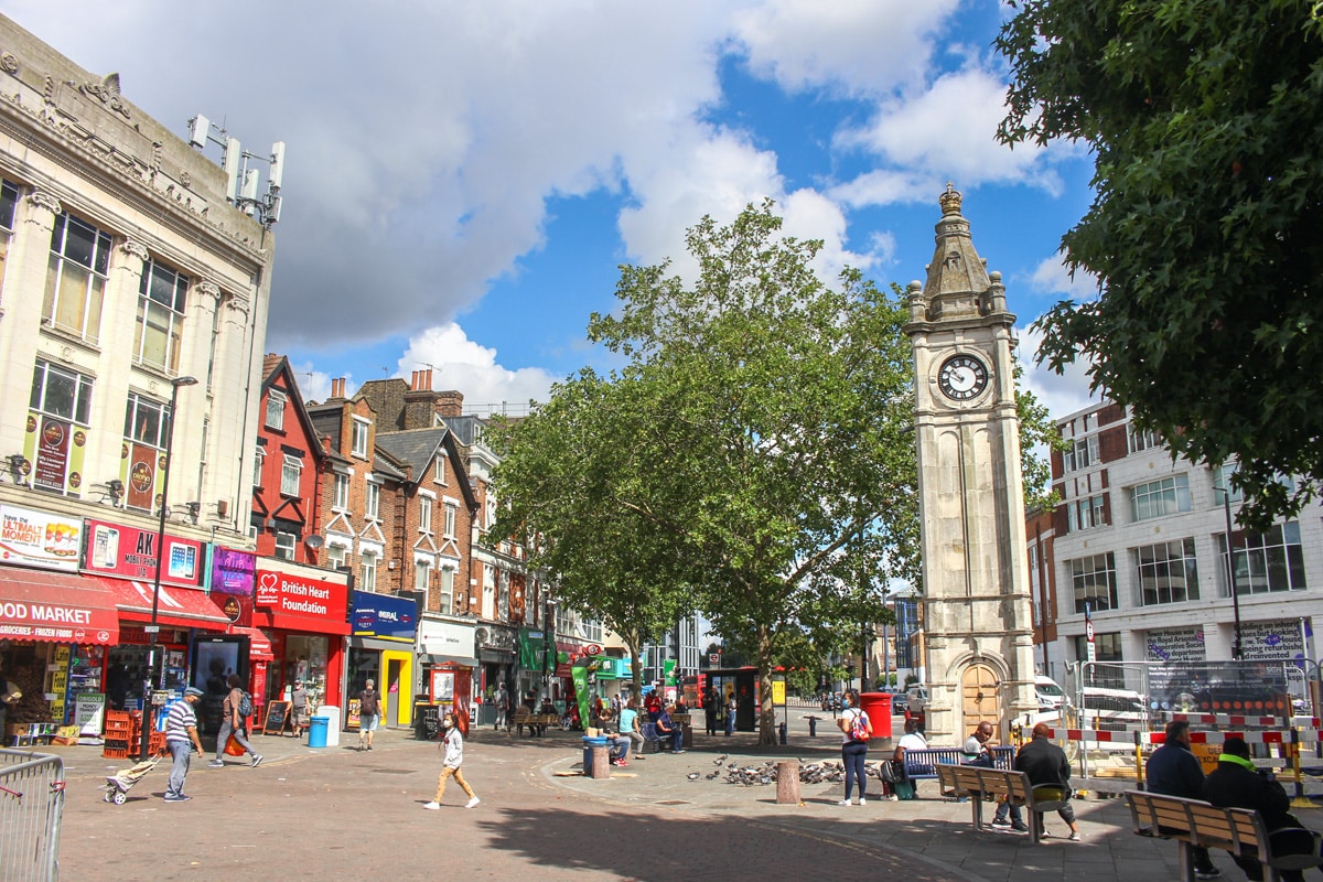 Lewisham high street on a sunny day. There are shoppers and the historic clock tower is in view.