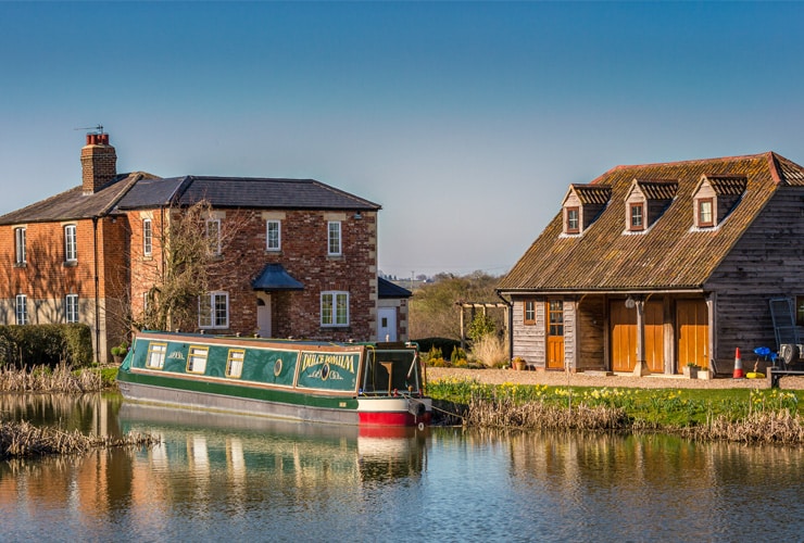 A canal boat is moored in front of a country house. Photograph taken in Devizes, Wiltshire.