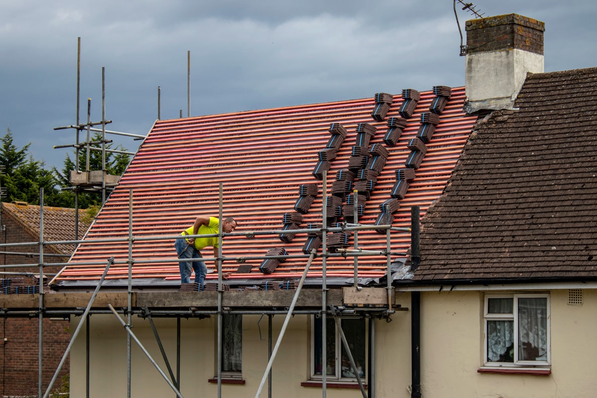 A man stands on scaffolding surounding a building. He is preparing to re-tile a roof.