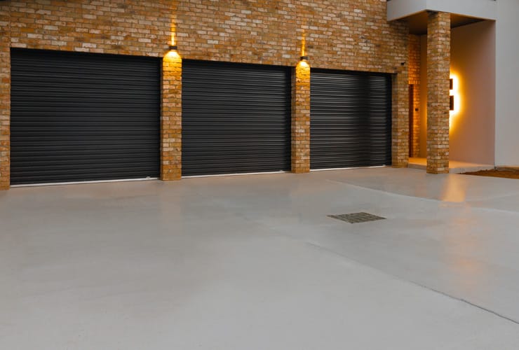 A freshley laid concrete driveway leads to three garage doors.