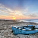 Turquoise blue fishing boat at sunrise on Bournemouth beach with the pier in the far distance.