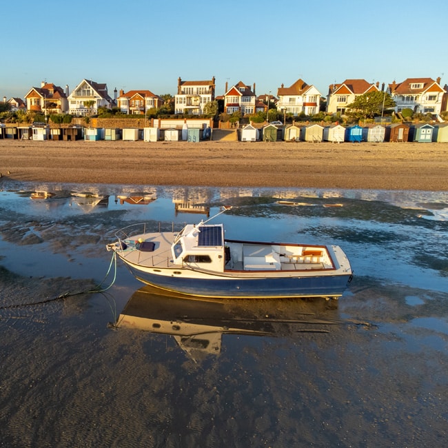 A boat in the sea near Southend beach at low tide. Photograph taken near Thorpe Bay during sunset, on a clear, autumn day.