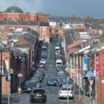 Red brick terraced housing, shops and businesses with a large domed mosque in the background. Photograph of Charlotte Street in Blackburn.