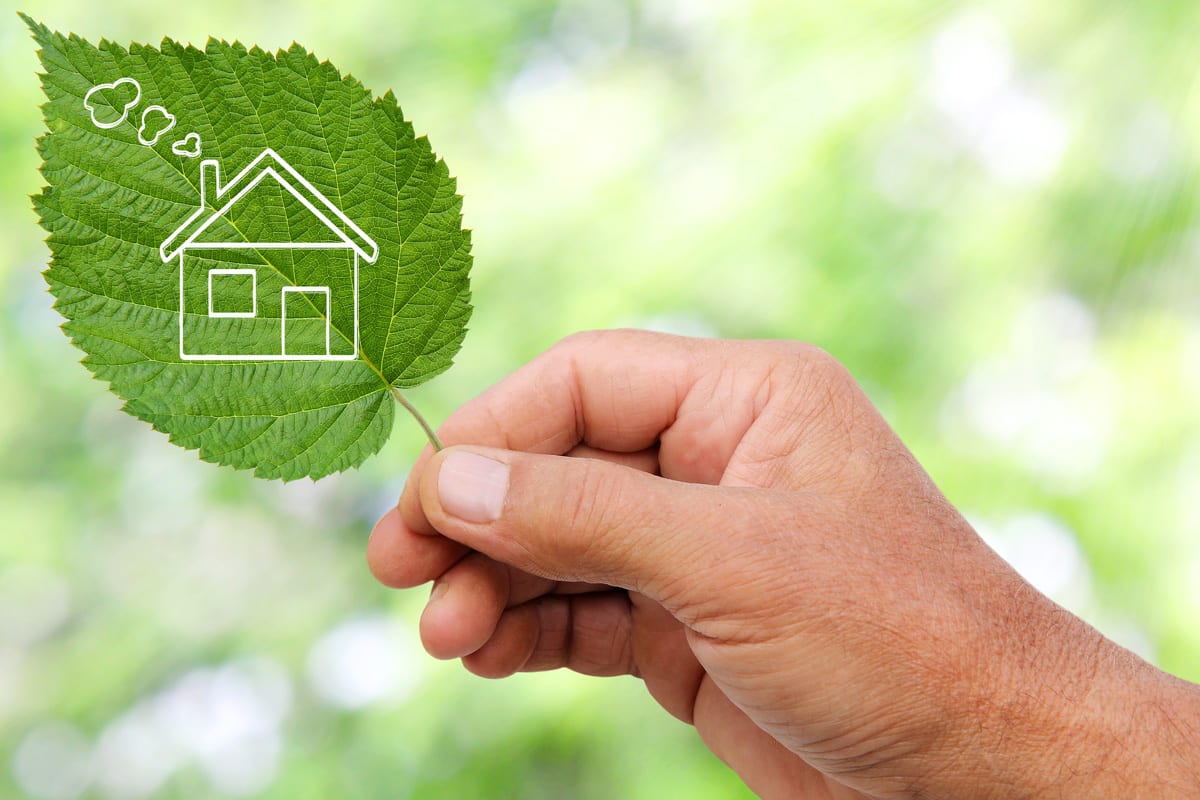 A hand holding a leaf with a picture of a house on it. Represents an ecologically friendly house.