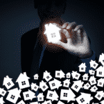 A businessman on dark background holding a glowing house icon with fingers.