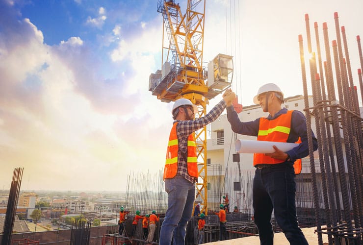 An architect and an engineer shake hands on an outdoor construction site.