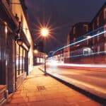 An illuminated high street of Harrow on the Hill with a passing bus and cars in motion.