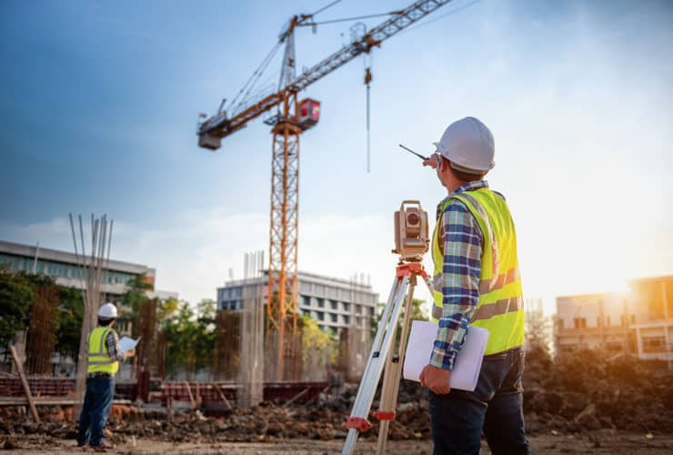 A surveyor stands on a construction site.