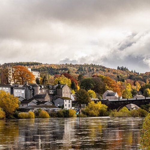 An autumnal scene of Perth in Scotland. The city is seen among red, yellow and orange trees
